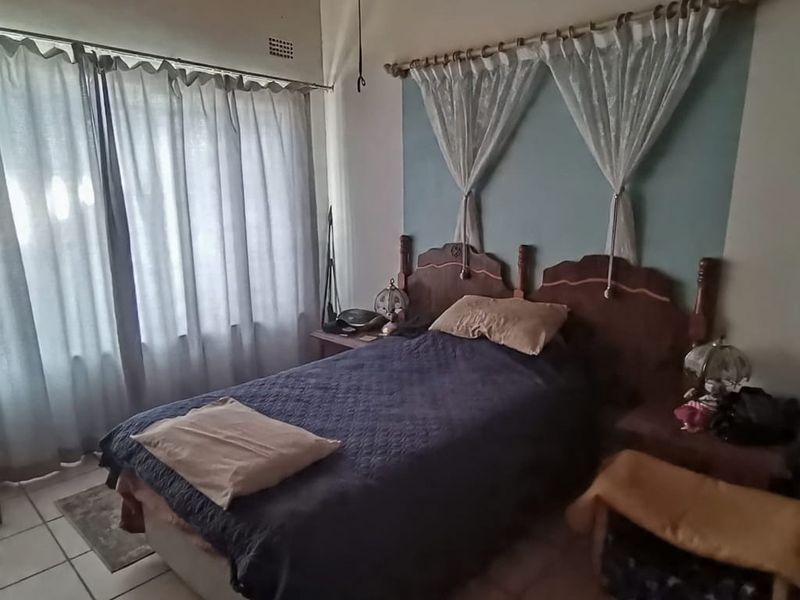 A bedroom featuring a timber ceiling, tiled flooring, and a large window, offering a functional space with potential for cosmetic updates.