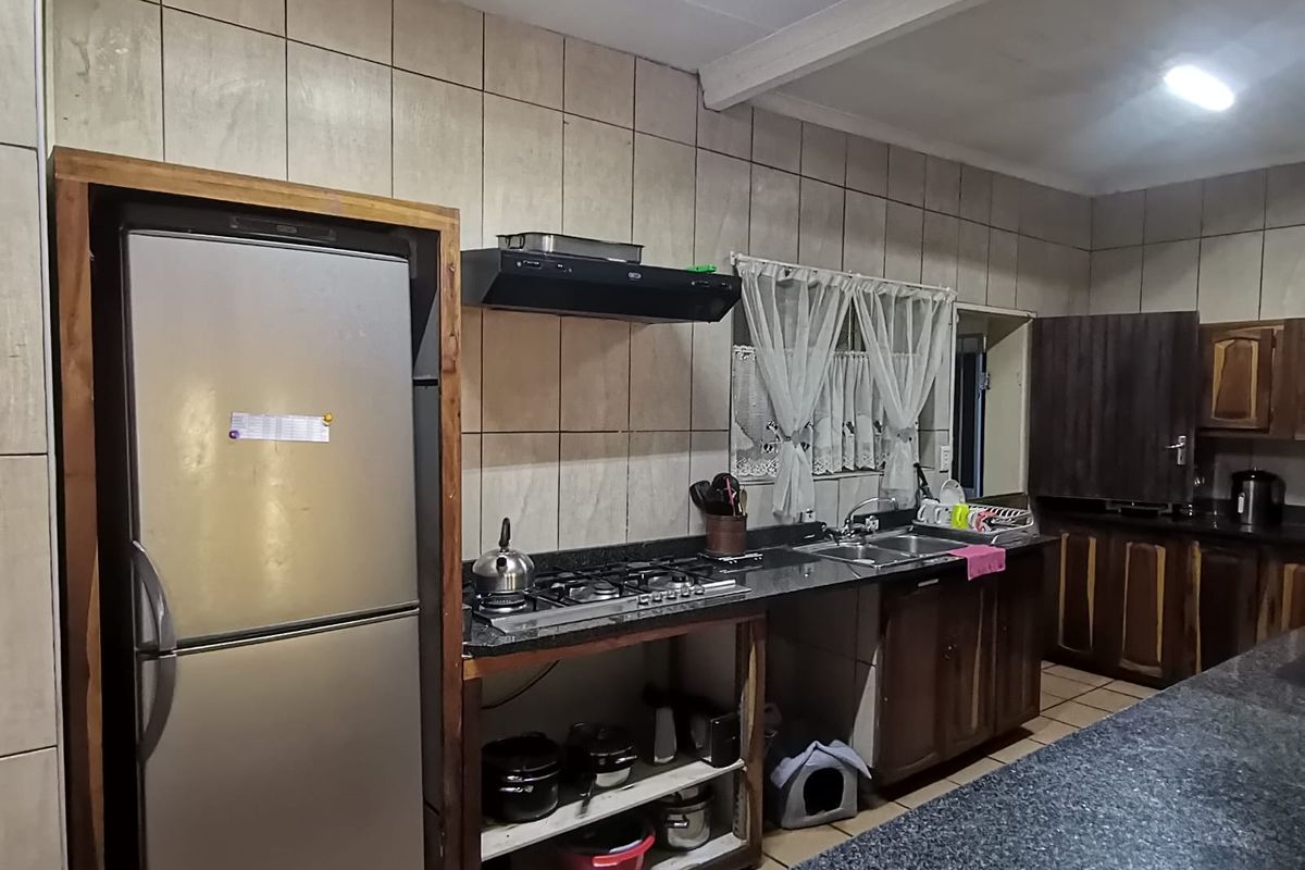 A functional kitchen featuring granite countertops, a gas hob, extractor fan, and double sink, with open-style cabinetry and tiled wall finishes.
