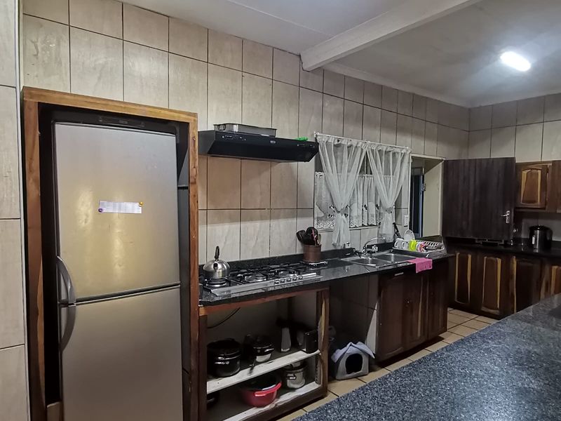 A functional kitchen featuring granite countertops, a gas hob, extractor fan, and double sink, with open-style cabinetry and tiled wall finishes.