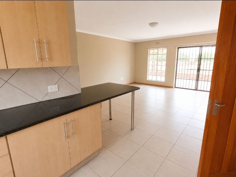 Spacious open-plan kitchen and living area featuring light wood cabinetry, granite countertops, tiled flooring, and access to an outdoor area through a sliding door.