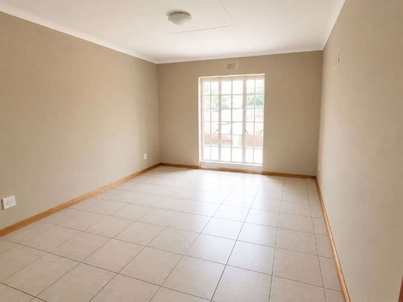 A bright, empty living room featuring neutral wall paint, tiled flooring, and a glass-paneled door providing natural light.