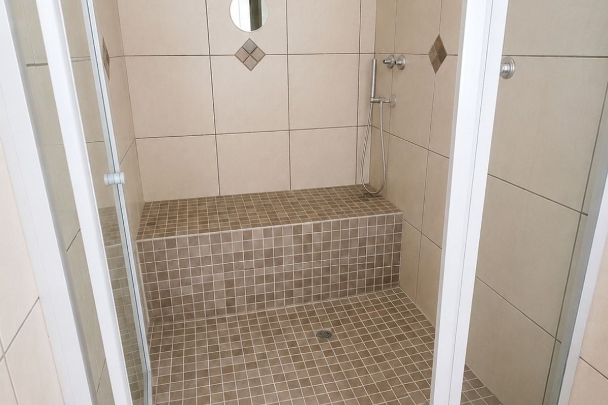 A clean walk-in shower featuring a built-in tiled bench, modern shower fixtures, and neutral wall and floor tiling.