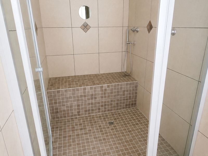 A clean walk-in shower featuring a built-in tiled bench, modern shower fixtures, and neutral wall and floor tiling.