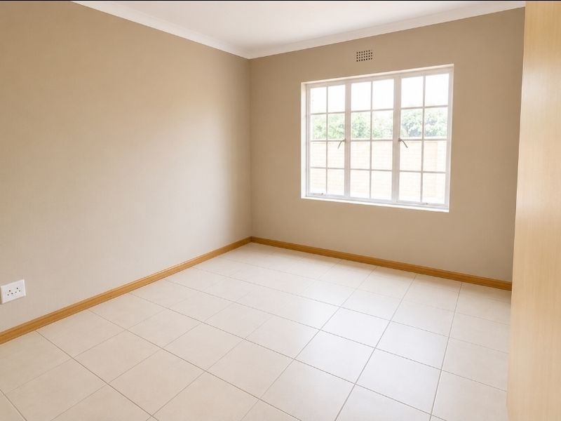 A bright, empty bedroom featuring neutral wall paint, tiled flooring, and a built-in cupboard, offering a clean canvas for personalization.