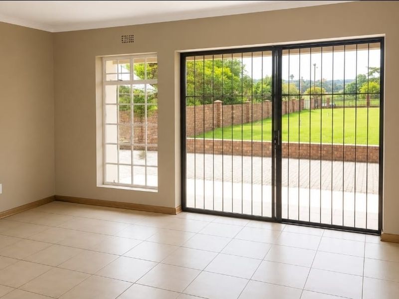A bright, empty living room featuring neutral tiled flooring, large sliding glass doors with security gates, and views of the garden.