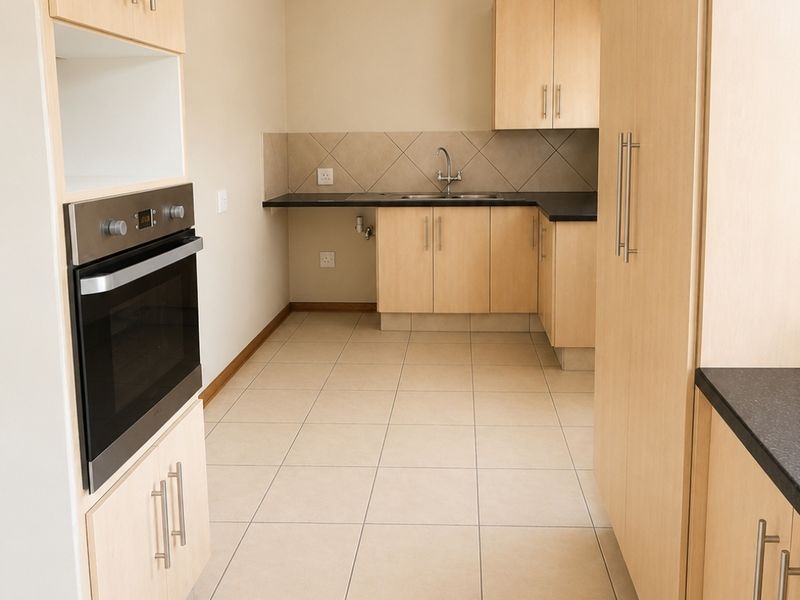 A clean, functional kitchen featuring light wood-tone cabinetry, dark countertops, tiled backsplash, and a built-in oven, presented in an empty, well-maintained state.