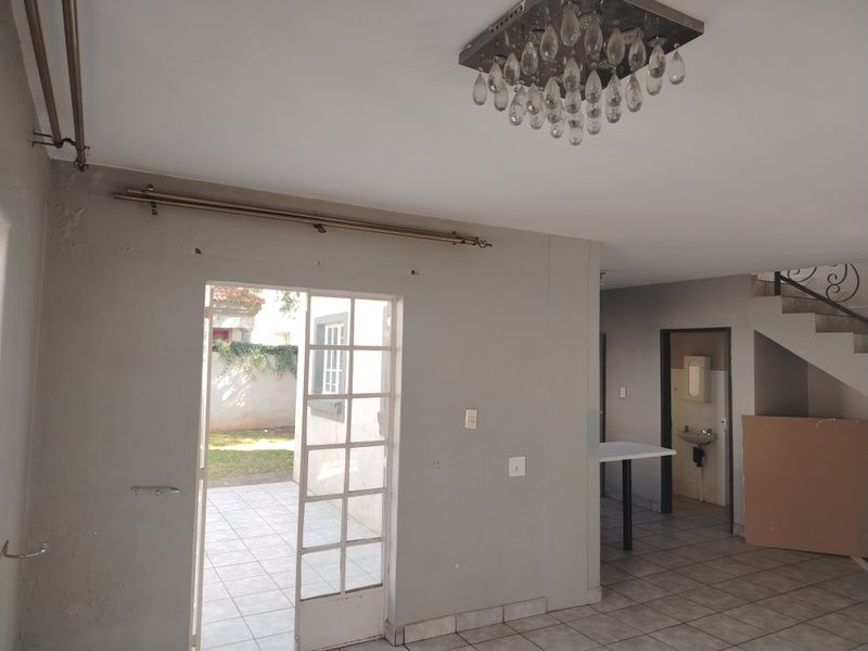 Open-plan living area featuring tiled floors, a crystal chandelier, and direct access to a rear patio, with an adjacent small wash area.