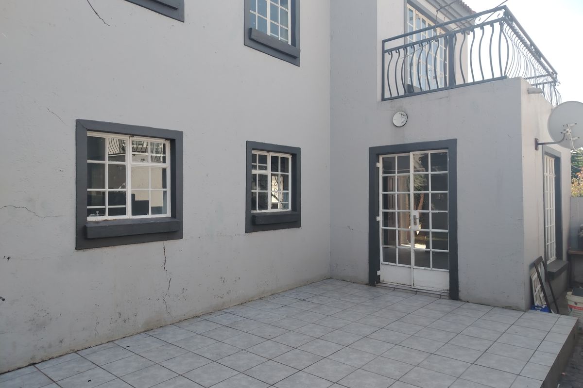 Rear exterior view of the townhouse featuring a tiled patio area, upper-level balcony with wrought iron railing, and grid-pattern windows.