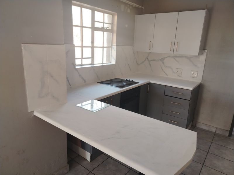 A compact kitchen featuring modern grey and white cabinetry, marble-effect countertops, an integrated electric hob and oven, and tiled flooring.