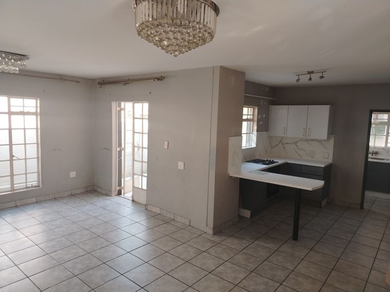 Open-plan living and kitchen area featuring tiled flooring, built-in cabinetry with marble-look splashback, breakfast bar, and decorative crystal chandeliers.