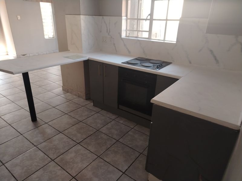 A functional kitchen featuring built-in oven, electric hob, marble-look backsplash, and a breakfast bar with tiled flooring throughout.