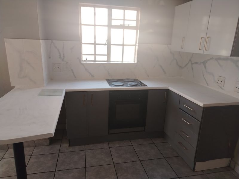A functional kitchen featuring grey cabinetry, marble-look splashbacks, built-in oven, electric hob, and tiled flooring with a breakfast nook extension.