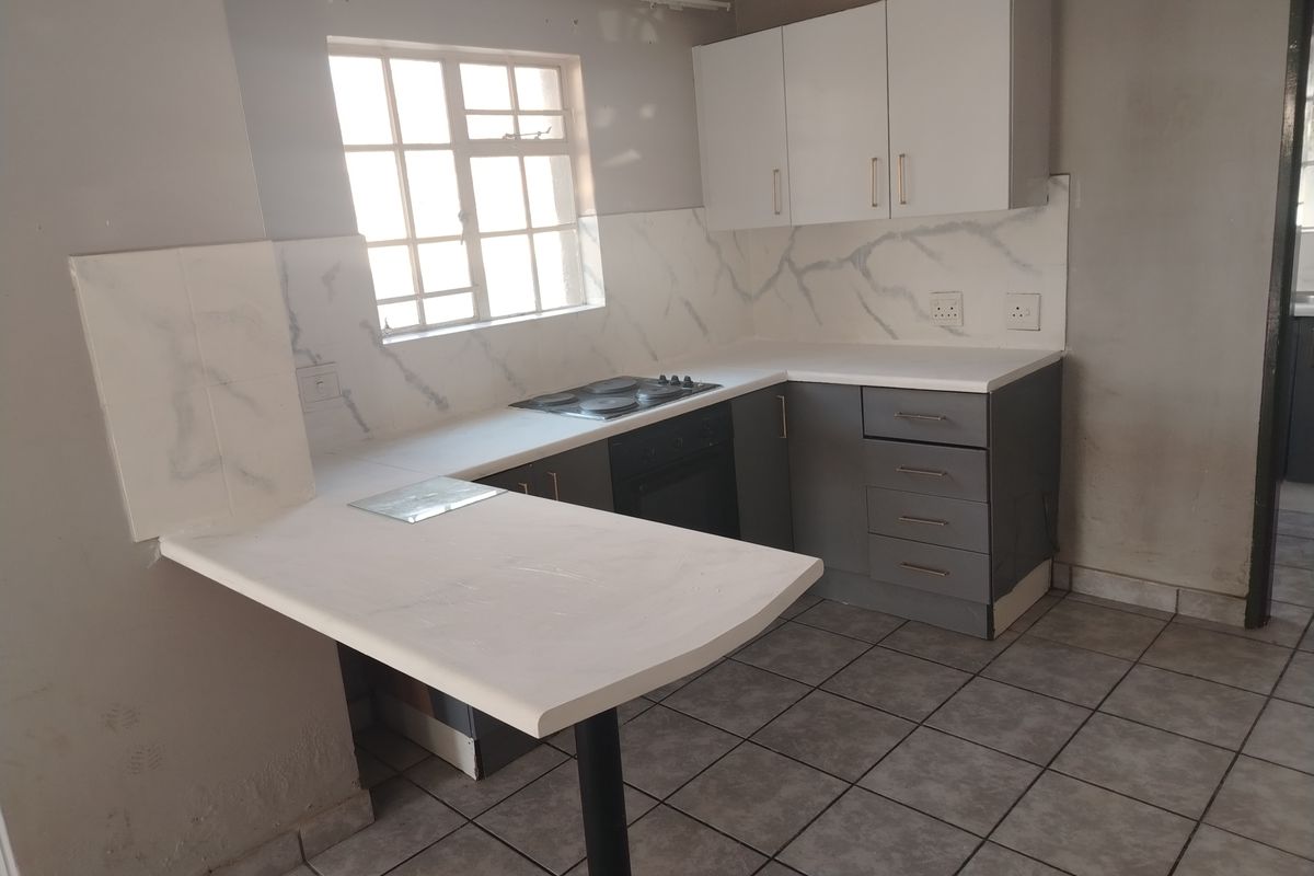 A compact kitchen featuring grey and white cabinetry, a built-in oven and hob, marble-look splashback, and a breakfast bar with tiled flooring.