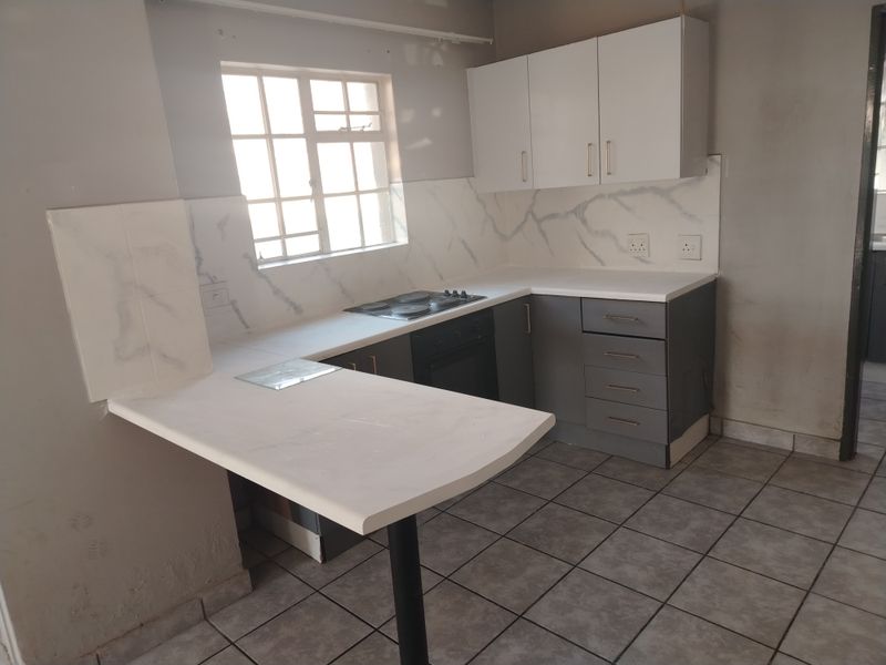A compact kitchen featuring grey and white cabinetry, a built-in oven and hob, marble-look splashback, and a breakfast bar with tiled flooring.