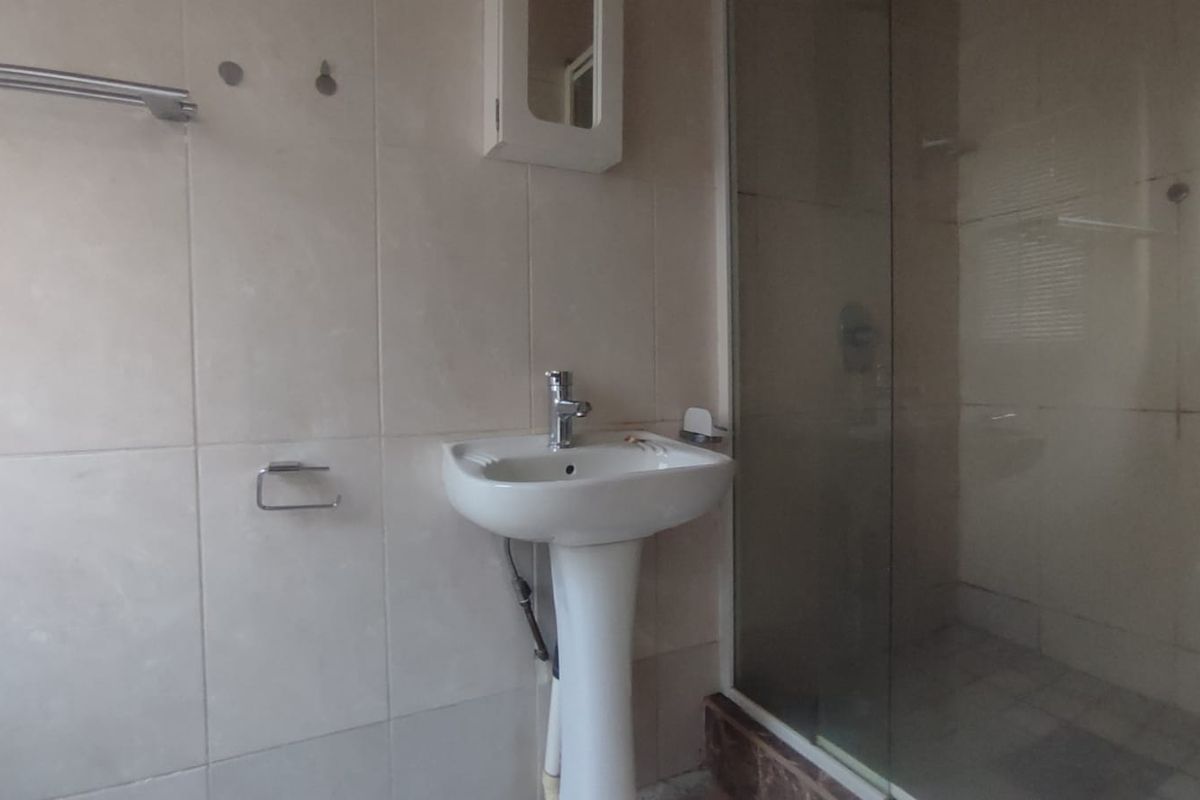 A functional bathroom featuring a pedestal washbasin, chrome fixtures, and a glass-enclosed shower with tiled walls.