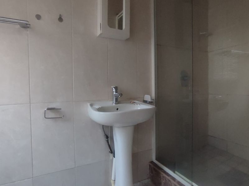 A functional bathroom featuring a pedestal washbasin, chrome fixtures, and a glass-enclosed shower with tiled walls.