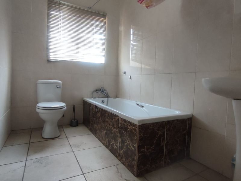 A functional bathroom featuring a bathtub with tiled surround, pedestal basin, and neutral wall and floor tiling.