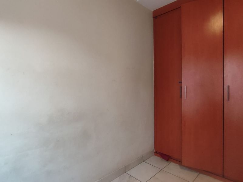 A vacant bedroom featuring tiled flooring and a large built-in wooden wardrobe with sliding doors.