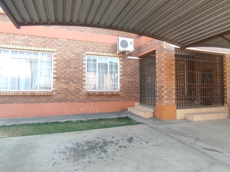 Front exterior view of the apartment featuring a brick facade, a covered carport, and a secure entrance with metal security gates.