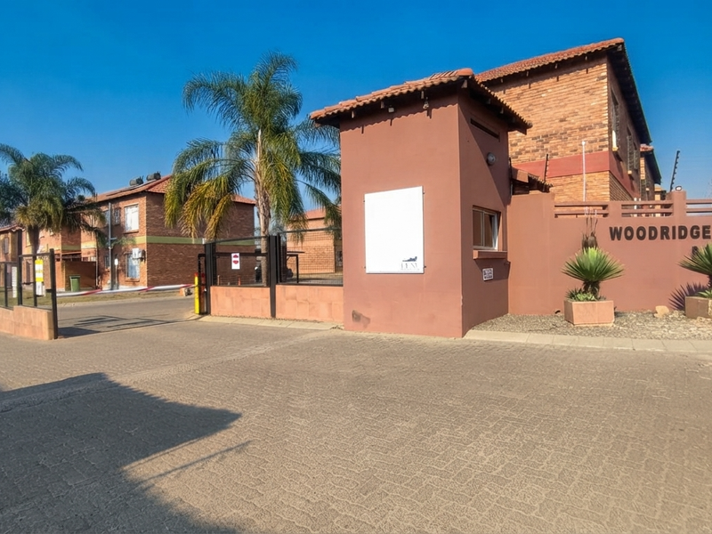 Front entrance view of the Woodridge apartment complex featuring a secure gated access point, brick facade buildings, and paved driveway.