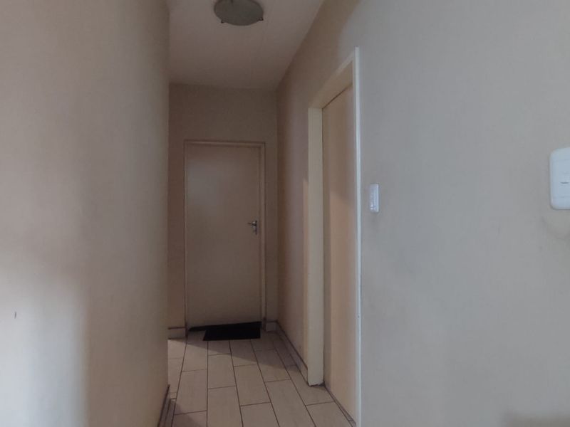 A simple, empty interior hallway featuring tiled flooring and neutral wall finishes, providing access to adjacent rooms.
