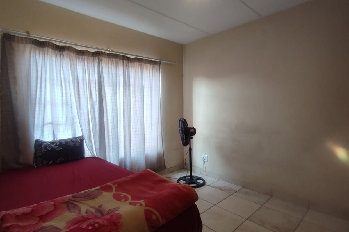 A bedroom featuring tiled flooring and a large window with a curtain rail. The walls show visible signs of staining and wear.