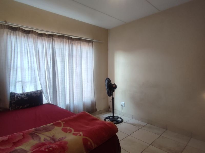 A bedroom featuring tiled flooring and a large window with a curtain rail. The walls show visible signs of staining and wear.