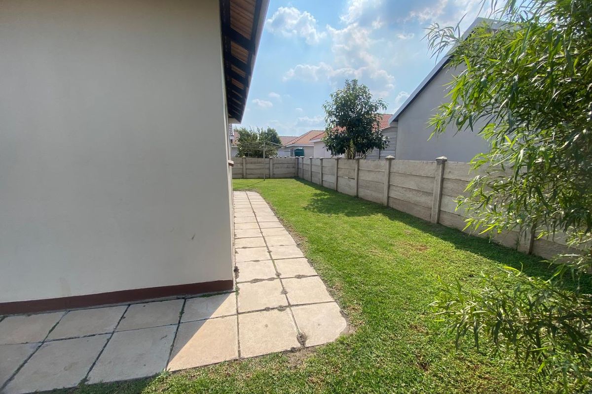 A side view of the property showing a paved walkway, a small lawn area, and a precast concrete boundary wall.
