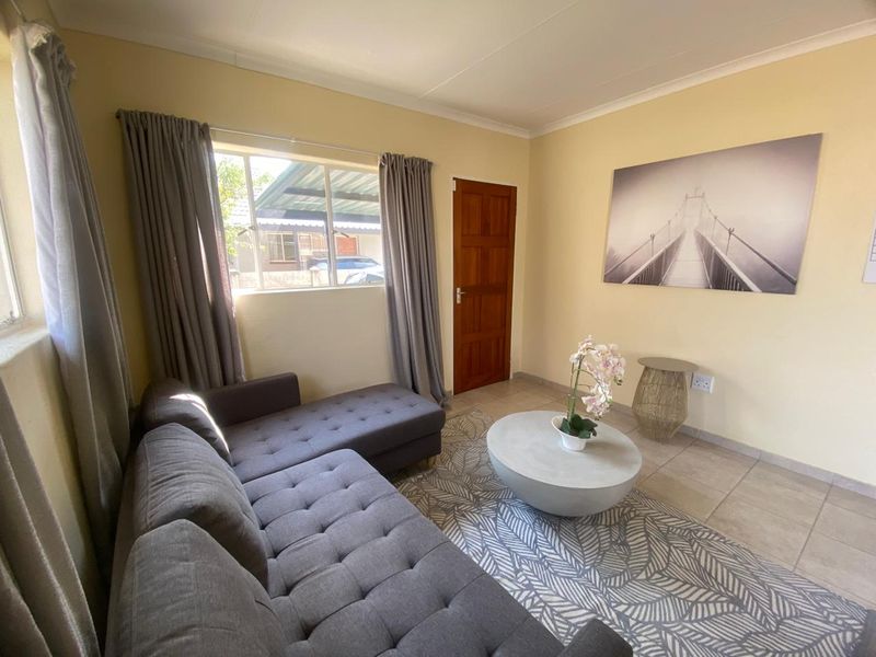 A cozy living room featuring tiled flooring, a timber door, and natural light through an aluminium-framed window.