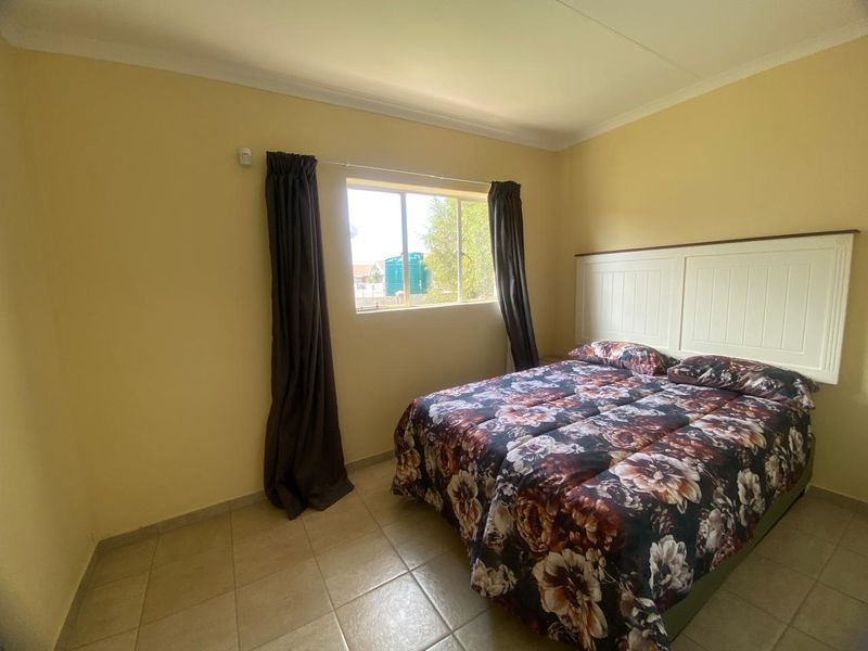 A functional bedroom featuring tiled flooring and a built-in headboard, offering a neutral space ready for personalization.