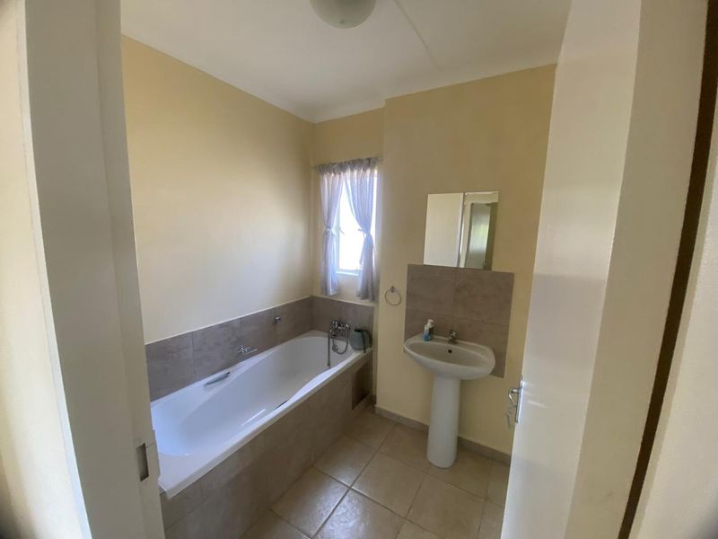 A functional bathroom featuring a pedestal basin, a built-in bathtub with tiled surround, and neutral wall finishes.