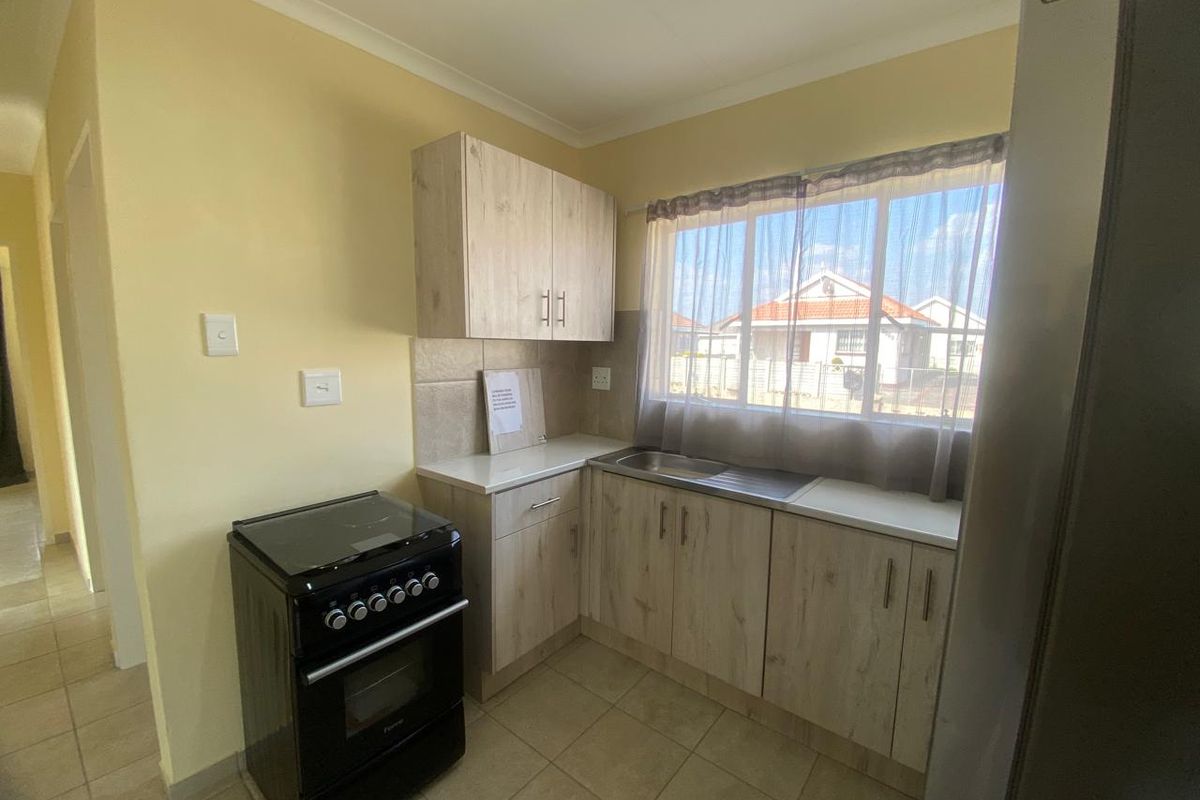 Compact kitchen featuring light wood-look cabinetry, tiled backsplash, stainless steel sink, and ceramic floor tiles with a functional layout.