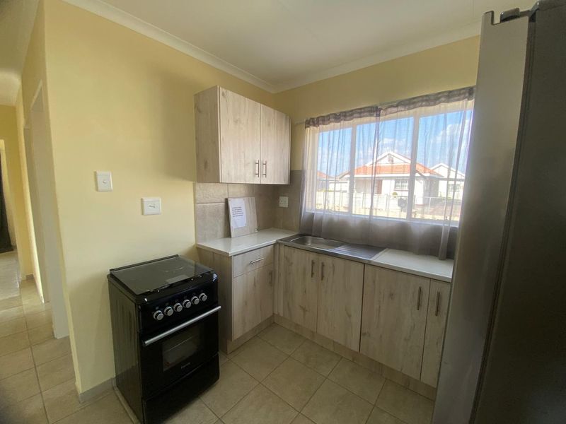 Compact kitchen featuring light wood-look cabinetry, tiled backsplash, stainless steel sink, and ceramic floor tiles with a functional layout.