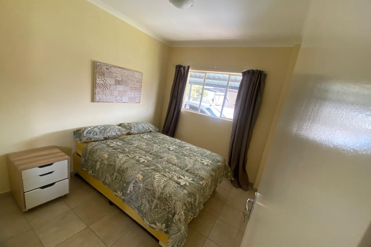 A functional bedroom featuring neutral wall tones, tiled flooring, and a window providing natural light.