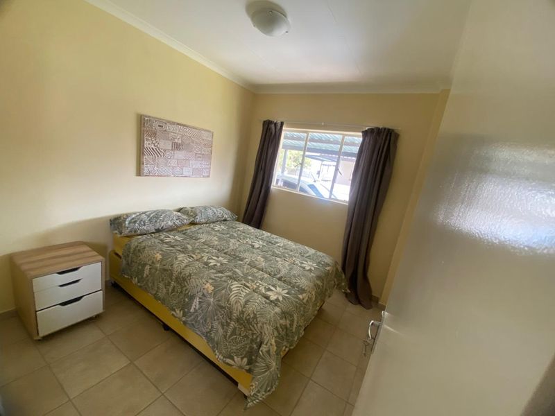 A functional bedroom featuring neutral wall tones, tiled flooring, and a window providing natural light.