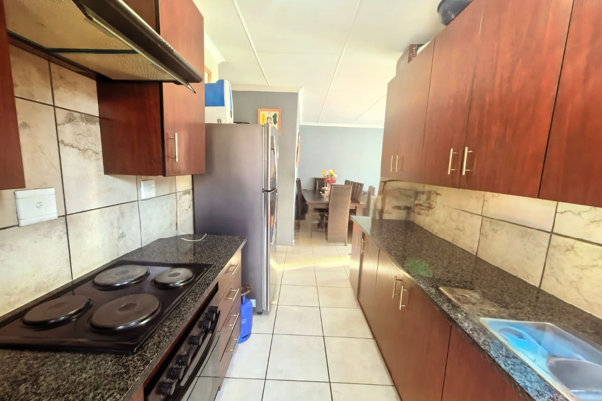 Functional kitchen featuring dark wood cabinetry, granite countertops, an electric hob, and a tiled backsplash, leading into an adjacent dining area.