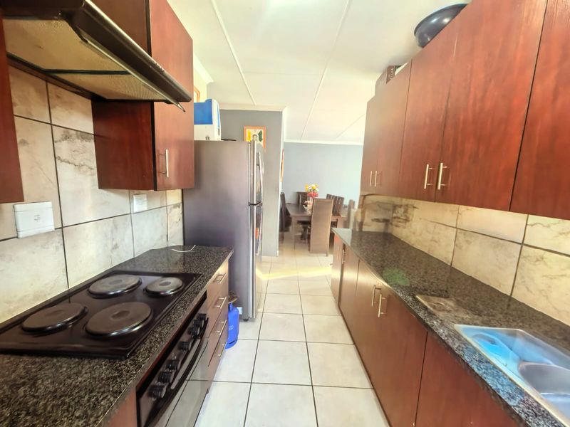 Functional kitchen featuring dark wood cabinetry, granite countertops, an electric hob, and a tiled backsplash, leading into an adjacent dining area.