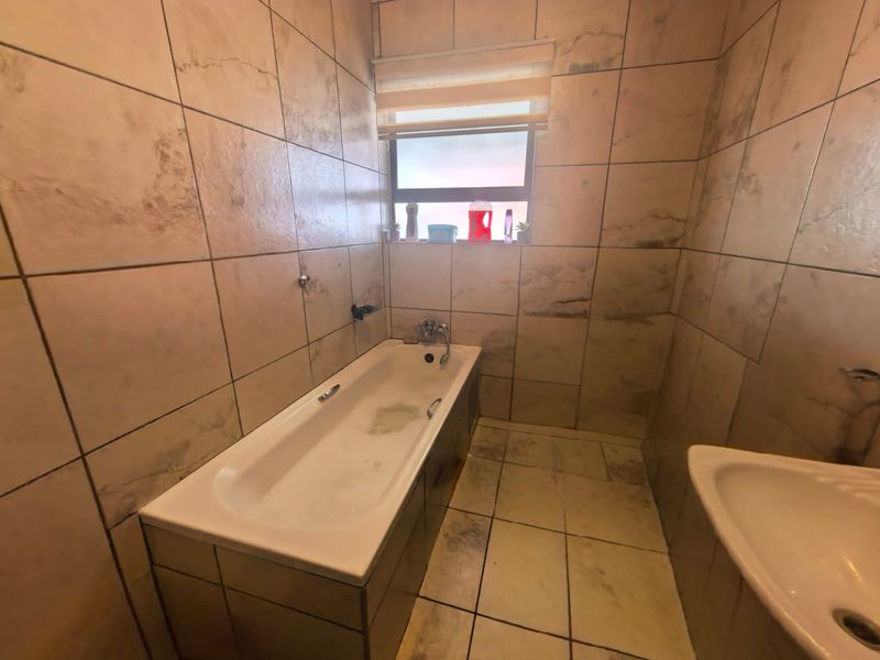 A bathroom featuring floor-to-ceiling wall tiles, a built-in bathtub, and a basin, requiring some maintenance and cleaning to restore its condition.