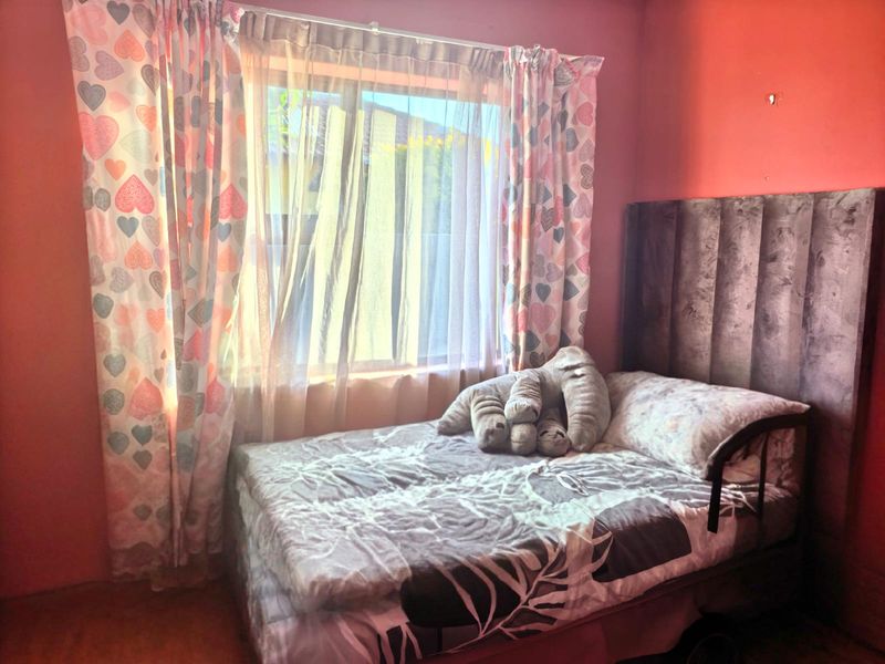 A bedroom featuring a window with curtains and a tall headboard, requiring cosmetic updates to the wall finishes.
