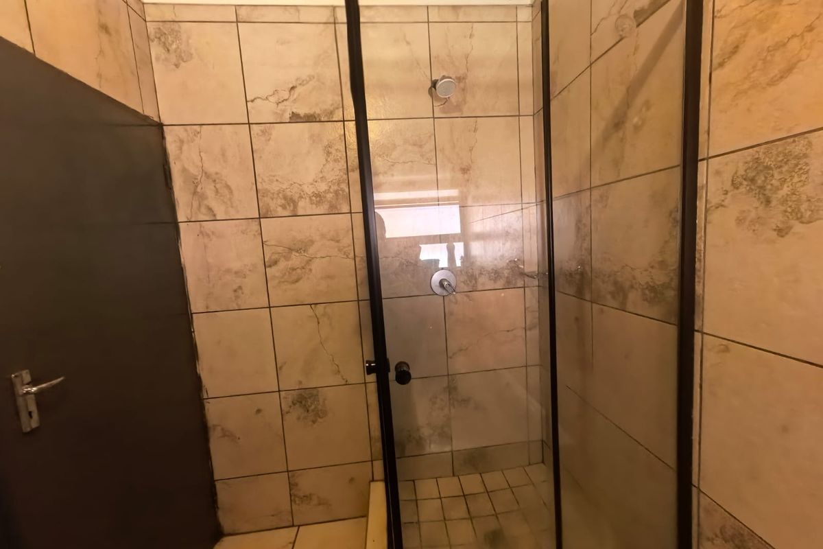 A functional bathroom shower area featuring a glass enclosure with a black frame and neutral-toned wall and floor tiling.