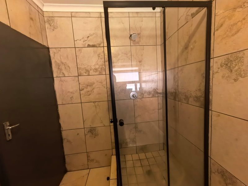 A functional bathroom shower area featuring a glass enclosure with a black frame and neutral-toned wall and floor tiling.
