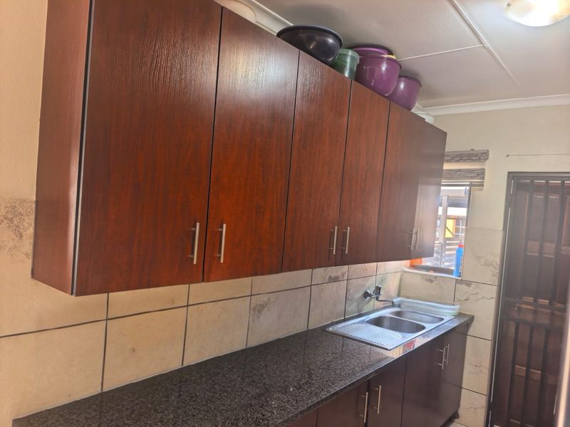 A functional kitchen featuring dark wood-look cabinetry, granite countertops, a stainless steel sink, and tiled backsplash with a secure exterior door.
