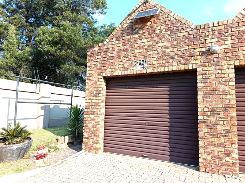 A well-maintained face brick garage featuring a secure roller shutter door, solar panel installation, and paved driveway access.