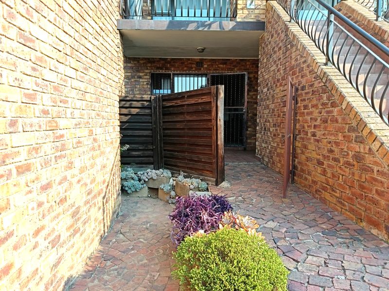 Exterior entrance area featuring exposed brick walls, a paved walkway, and a metal staircase leading to an upper level with security gate access.