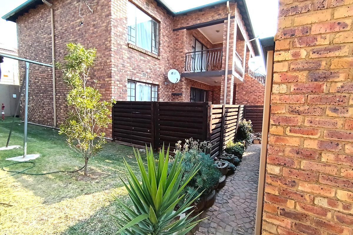 Rear view of a face brick apartment building featuring a private balcony, paved walkway, and small garden area.