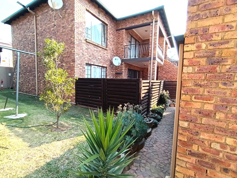 Rear view of a face brick apartment building featuring a private balcony, paved walkway, and small garden area.