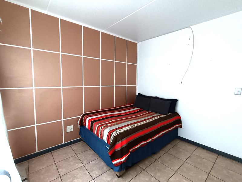 A bedroom featuring tiled flooring and a decorative paneled feature wall, requiring minor repairs to exposed electrical wiring.