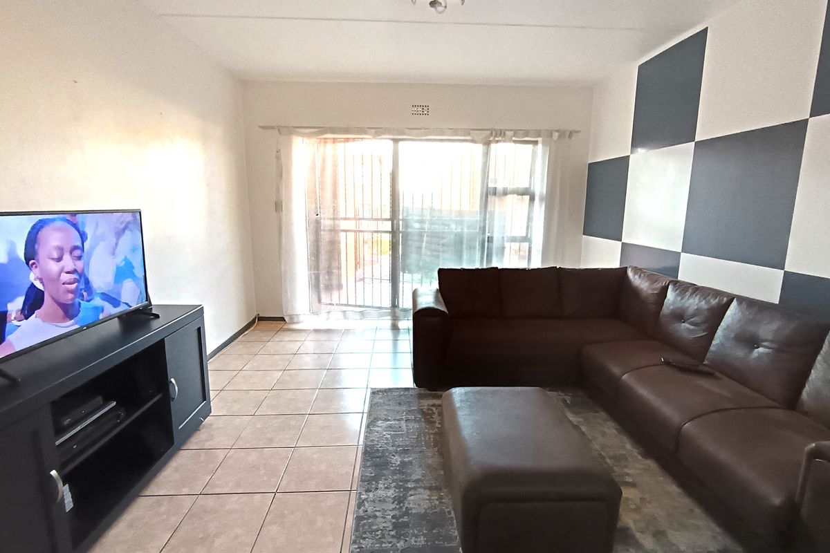 A living room featuring ceramic floor tiles and a sliding glass door with a security gate, providing access to the exterior.
