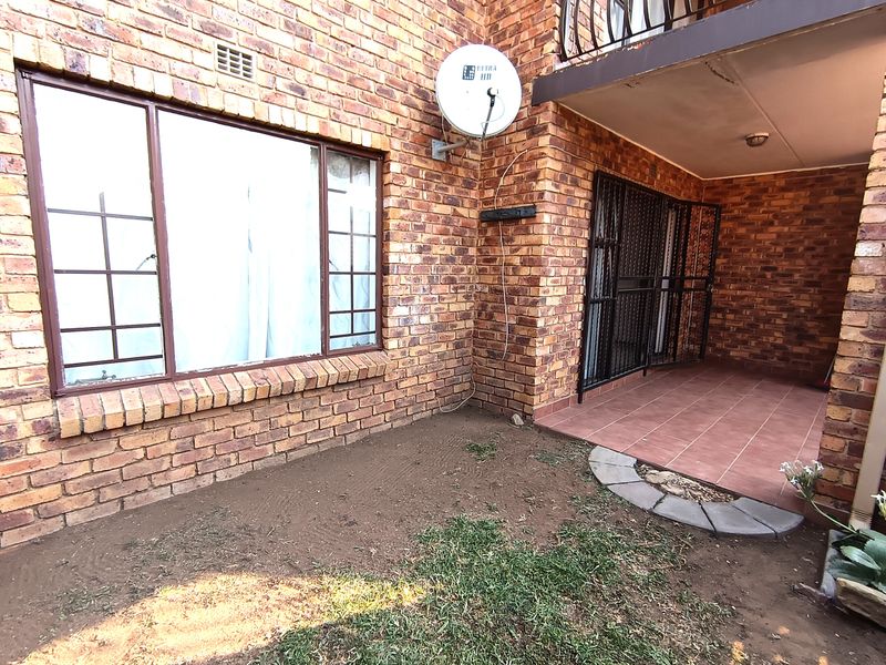 Rear exterior view of the apartment featuring a face brick facade, a tiled patio area, and a small garden space.
