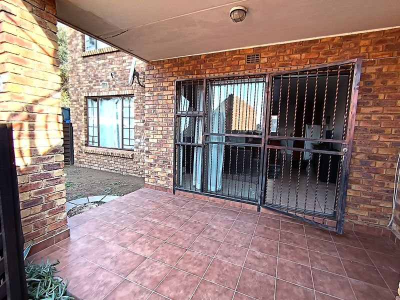A covered patio area featuring face brick walls, tiled flooring, and a security gate leading into the apartment interior.